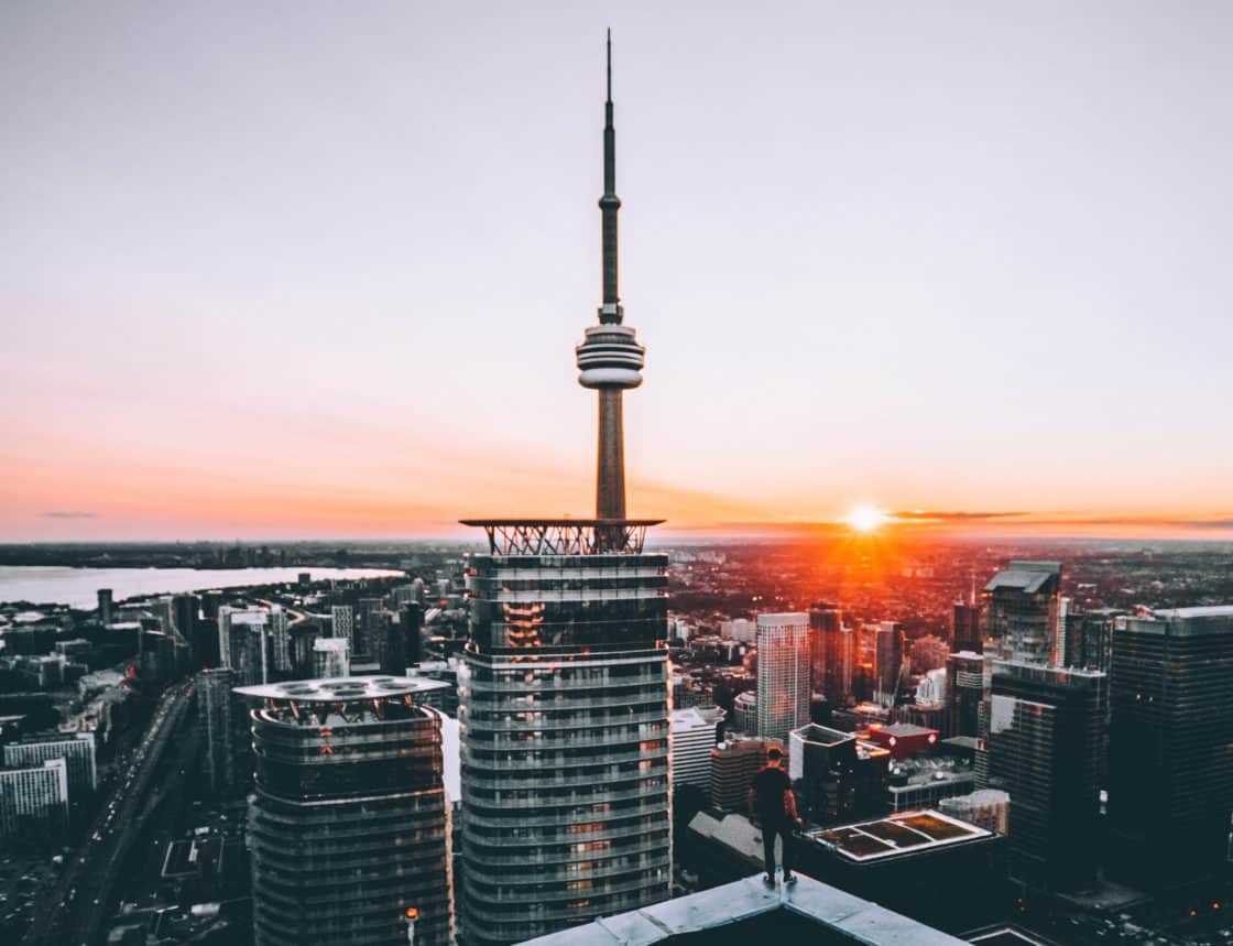 Mann steht auf Hochhaus und blickt über die Skyline Torontos in den Sonnenuntergang