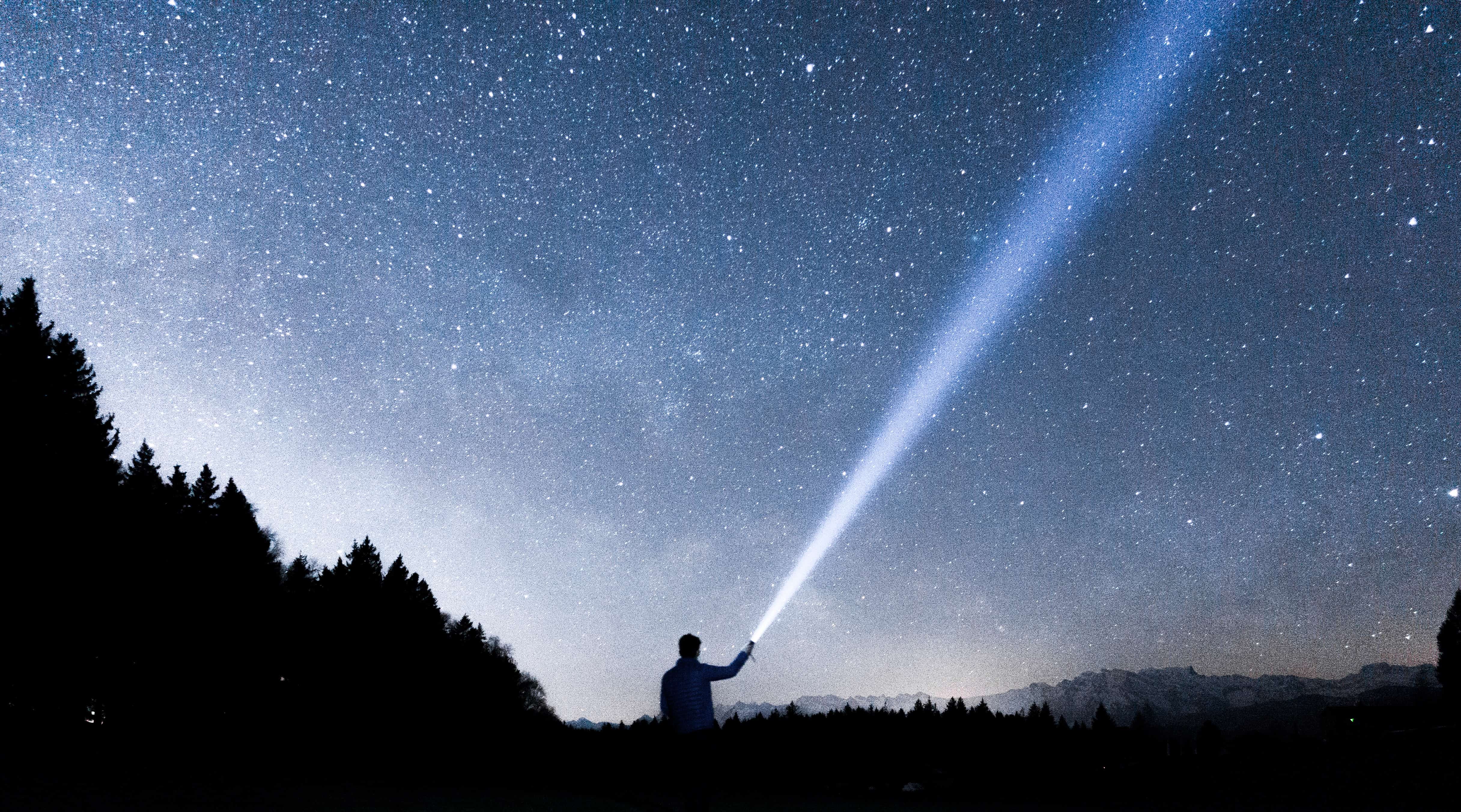 Mann mit Taschenlampe vor Sternenhimmel