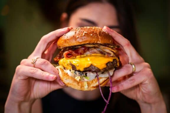 Eine Person hält einen frischen Burger vor ihr Gesicht.