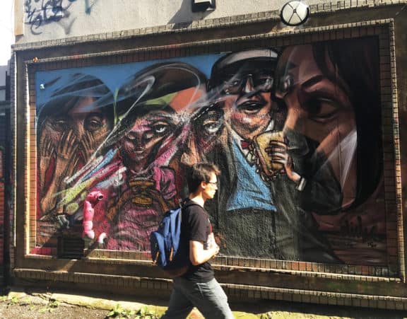 Junger Mann mit Rucksack läuft durch die Graffiti Alley