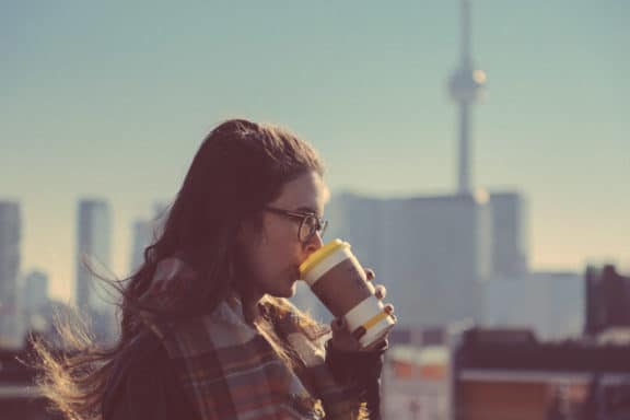 junge Frau mit Kaffe in der Hand, CN Tower im Hintergrund