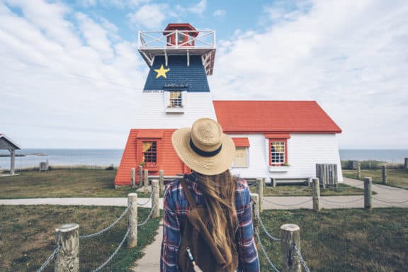 Frau vor Leuchtturm mit Acadian Flagge in Grande Anse, New Brunswick