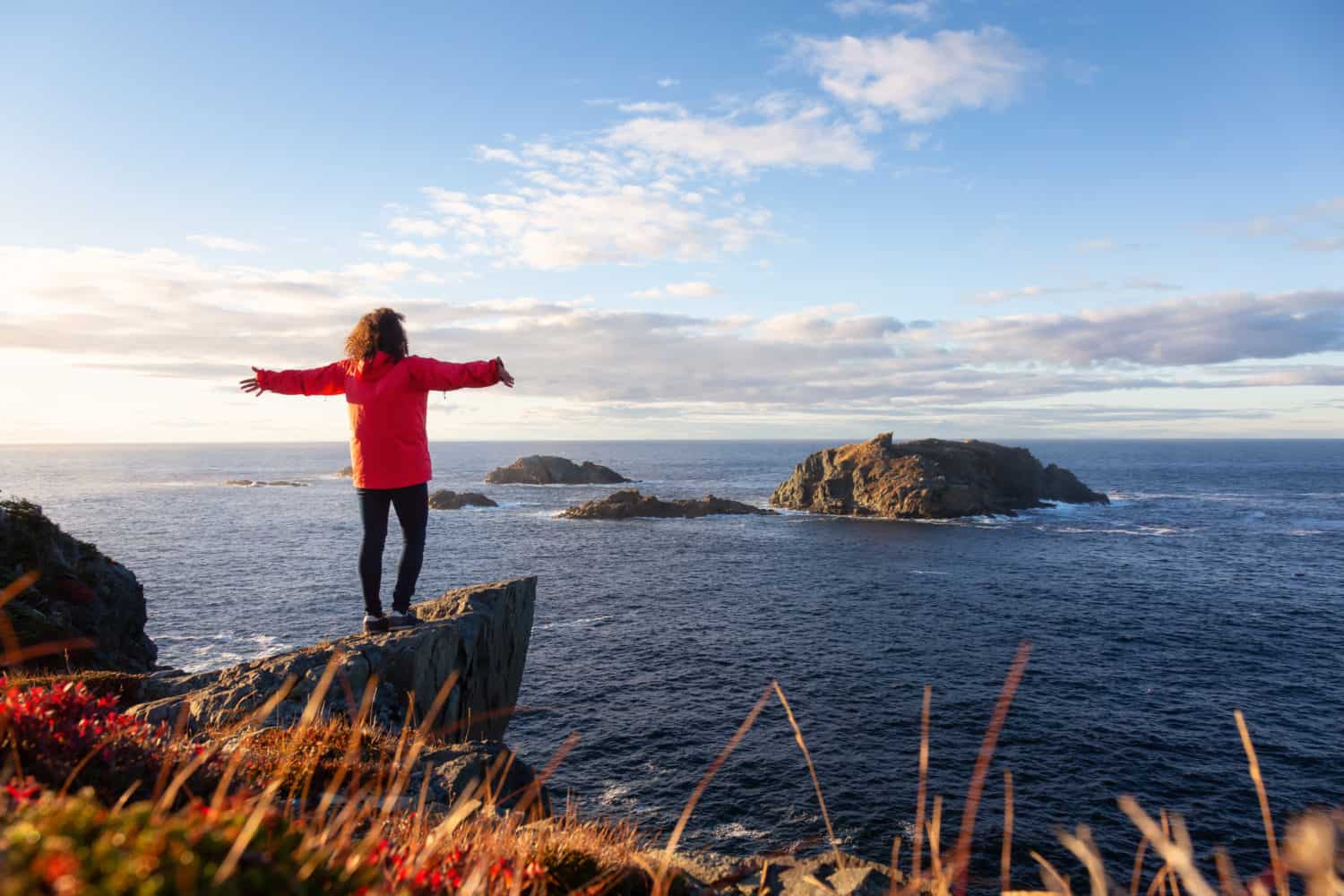 Twillingate, Neufundland und Labrador, Kanada. Frau steht auf einem Felsen und streckt die Arme aus. Dahinter ist das Meer.