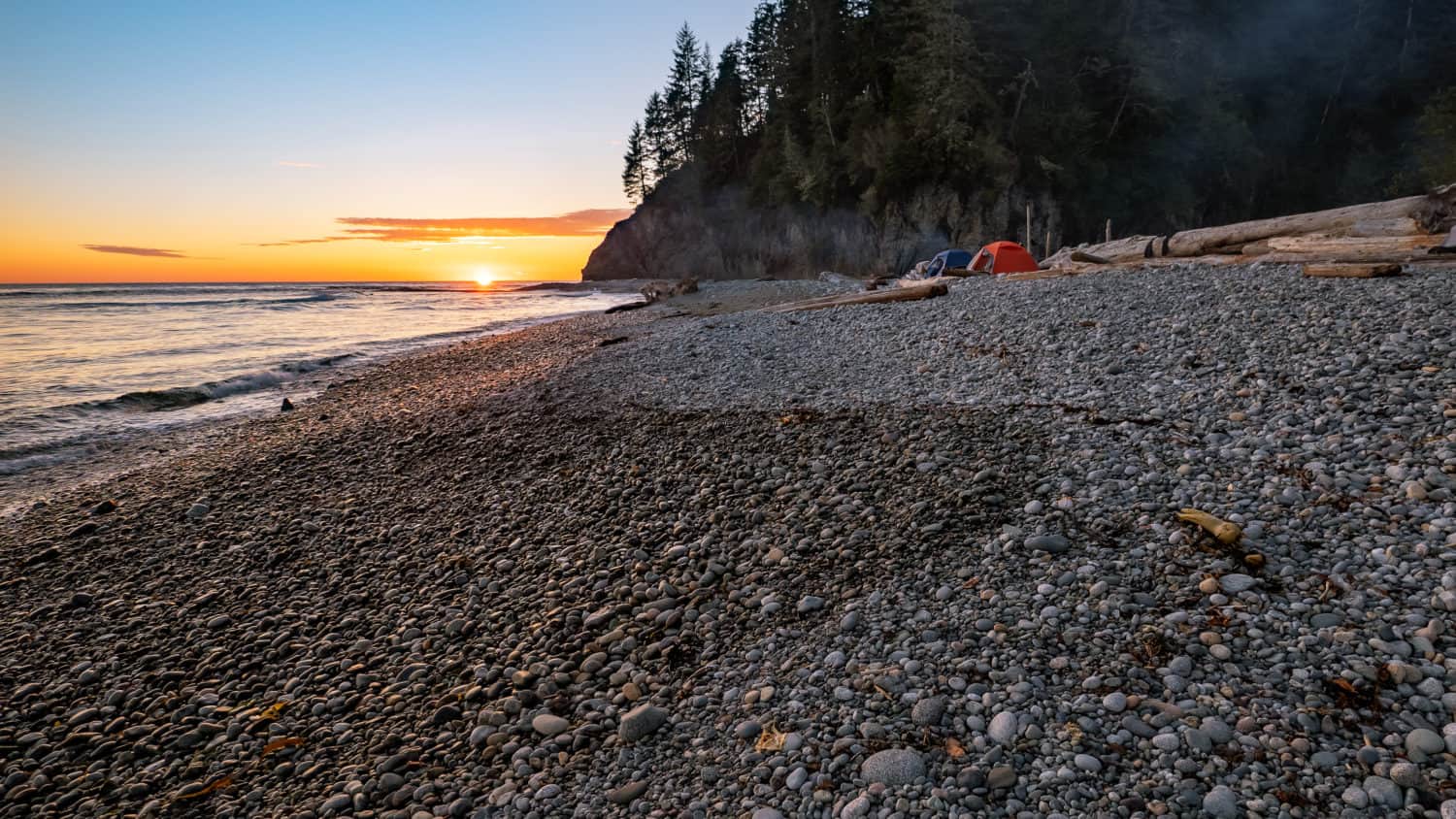 West Coast Trail, British Columbia auf Vancouver Island in Kanada. Zelte am Strand mit Felsen im Hintergrung und Sonnenuntergang.