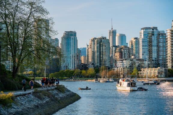 Gruppe joggt entlang eines Flusses in Vancouver. Vor ihnen liegt die Skyline der Stadt.