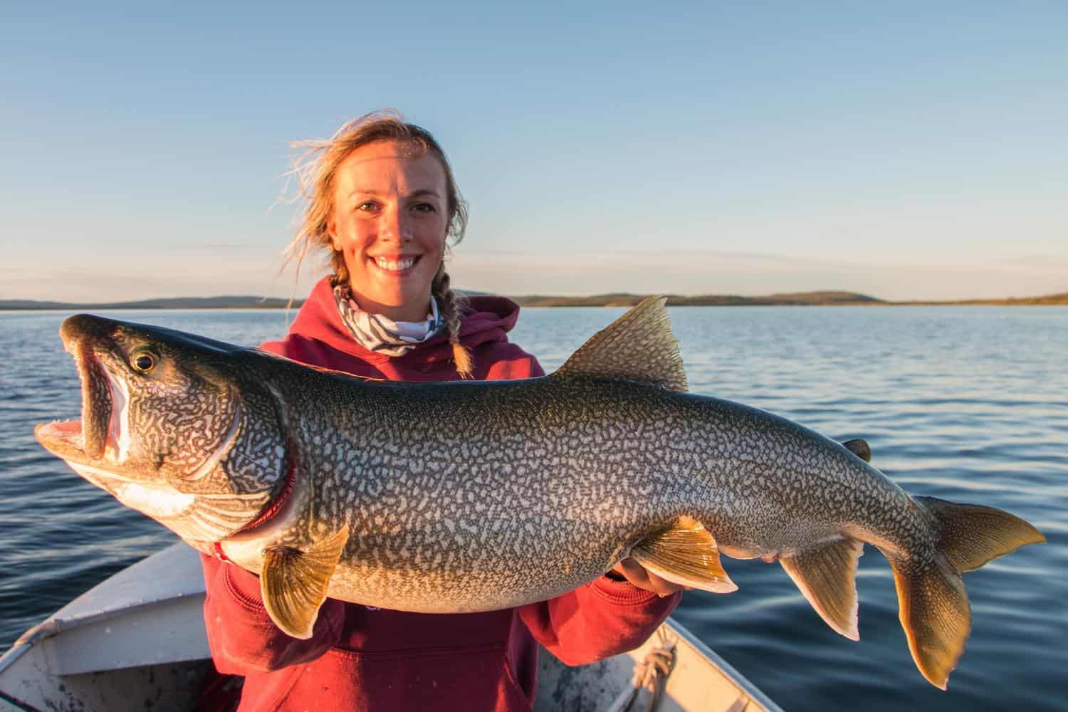 Frau hält riesigen Fisch in die Kamera, den sie während der Mitternachtssonne in den Northwest Territories geangelt hat