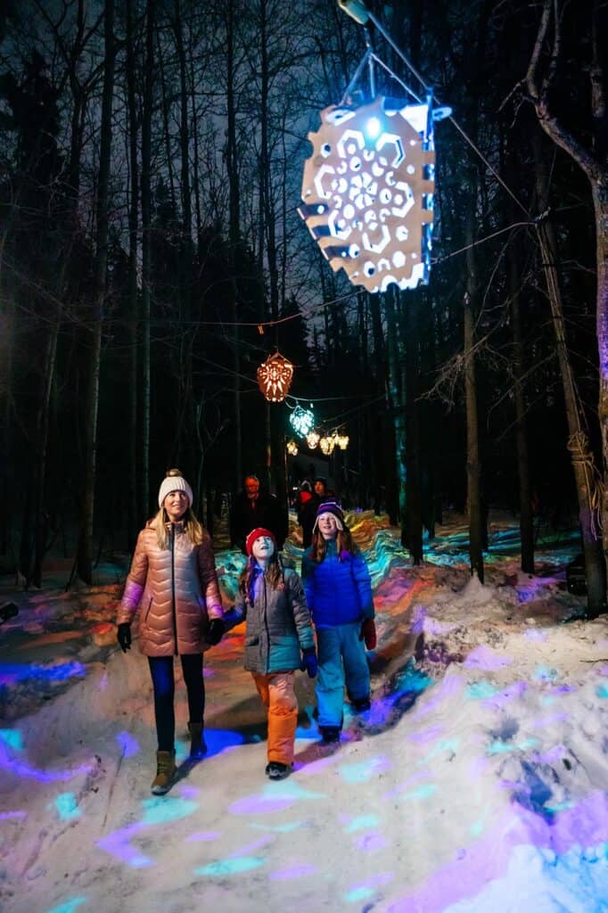 Eine Familie blickt auf bunte Lichter, während sie nachts durch einen Waldweg geht
