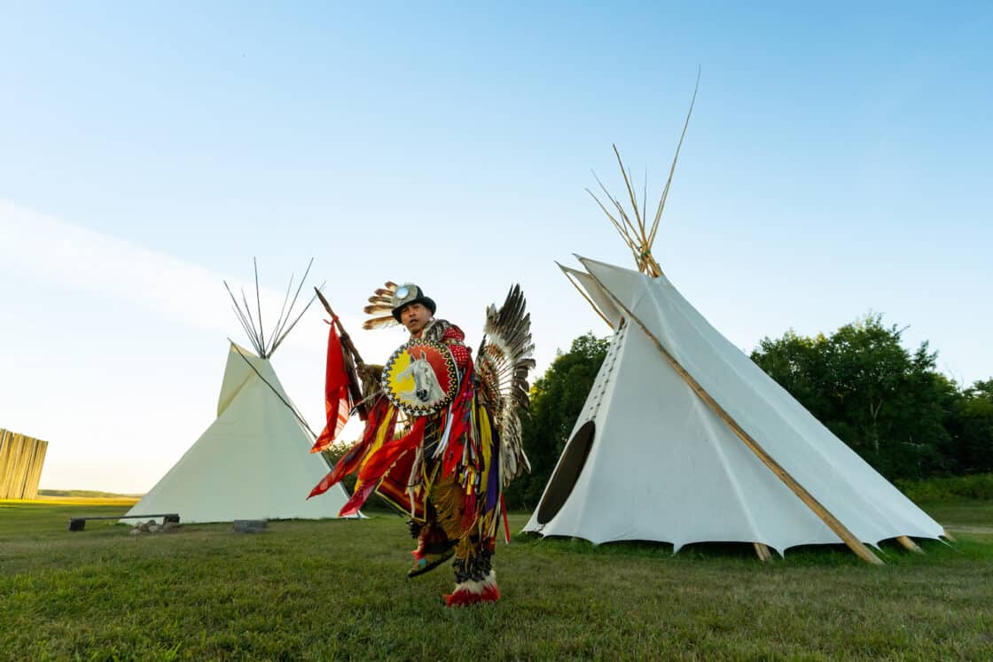 Tänzer der First Nations tanzt in traditioneller Kleidung in Saskatchewan. Im Hintergrund sind Tipis.