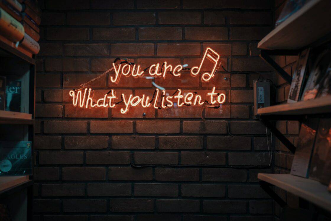 Orangener Neon Schriftzug "You are what you listen to" an der Wand