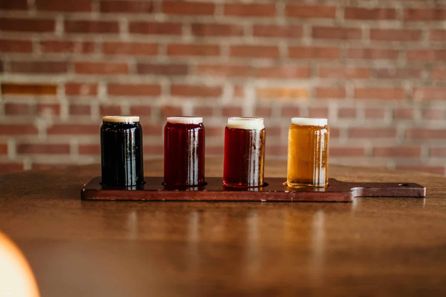 Vier verschiedene Biere stehen auf einem Holztablett. 
