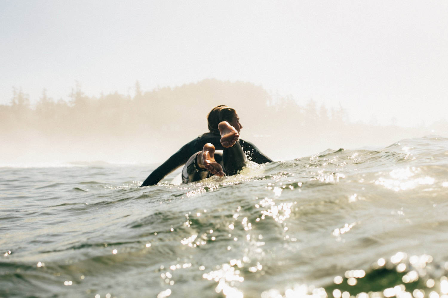 Person liegt auf Surfbrett und Paddelt durch das Meer.
